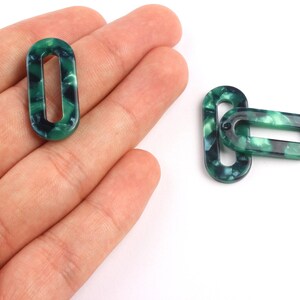 May include: Oval-shaped green and black marbled acrylic links. Two links are shown, one held in a hand and two others on a white surface. The links have a hollow centre and are suitable for jewellery making.