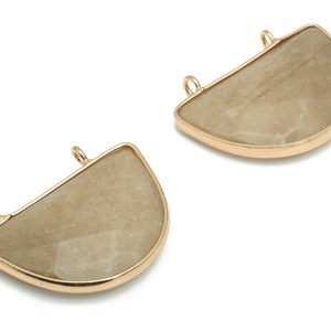 May include: Two gold-toned metal half-circle pendants with a beige stone inlay. The pendants have two small loops at the top for attaching to a necklace or bracelet.