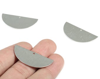 May include: Silver-colored, half-moon shaped metal charms with a brushed texture. Each charm has a small hole near the top edge. One charm is held in a hand, with two others scattered nearby. These are suitable for jewelry making.
