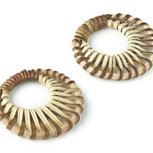 Puede incluir: Dos anillos tejidos hechos de materiales naturales marrones y beige. Los anillos son redondos y tienen un patrón decorativo.