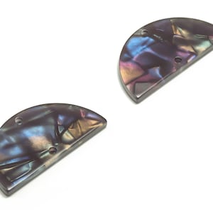 Może przedstawiać: Dwa półokrągłe guziki w kolorze czarnym z iryzującym wykończeniem, z trzema otworami każdy.