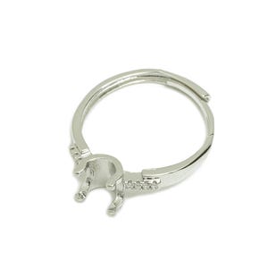 Könnte beinhalten: Silberring mit einer Krappenfassung für einen Stein. Der Ring hat ein dekoratives Band mit kleinen klaren Steinen.