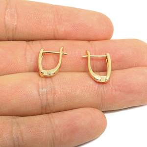 Peut inclure: Une paire de boucles d'oreilles créoles dorées. Chaque boucle d'oreille a une forme rectangulaire incurvée avec une fermeture à charnière. Les boucles d'oreilles sont présentées sur un fond neutre.