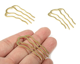May include: Three gold-colored hair combs with a wavy design. One comb is held in a hand, while two others are placed on a white surface. The combs have three tines each, and the overall design is simple and elegant.