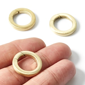 Peut inclure: Trois fermoirs circulaires dorés avec une ouverture à charnière. Les fermoirs sont en métal mat et sont présentés sur un fond blanc. Ces fermoirs sont utilisés pour la fabrication de bijoux et autres projets d'artisanat.