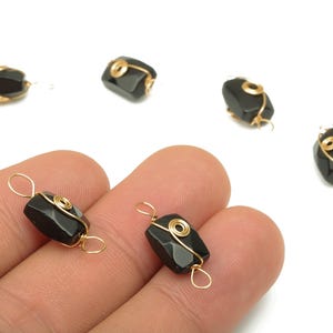 May include: Black, faceted gemstone beads with gold wire wrapping. The beads are rectangular with rounded edges and are suspended by gold wire loops. The beads are displayed on a white background.