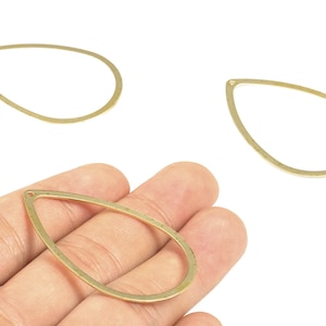 Könnte beinhalten: Drei goldfarbene, tropfenförmige Schmuckanhänger. Einer wird in einer Hand gehalten, während zwei weitere separat angezeigt werden. Diese Anhänger sind ideal für die Herstellung von Ohrringen, Anhängern oder anderen Schmuckdesigns.