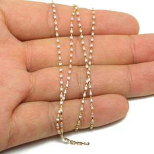 Könnte beinhalten: Zarte goldfarbene Halskette mit rechteckigen weißen Akzenten. Die Kette liegt auf einer Hand, wodurch das filigrane Design zur Geltung kommt. Die Halskette ist ein feines Schmuckstück, geeignet für den Alltag oder besondere Anlässe.