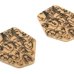 May include: A pair of beige resin earrings with a hexagonal shape. The earrings are decorated with a black and white line drawing of multiple faces.