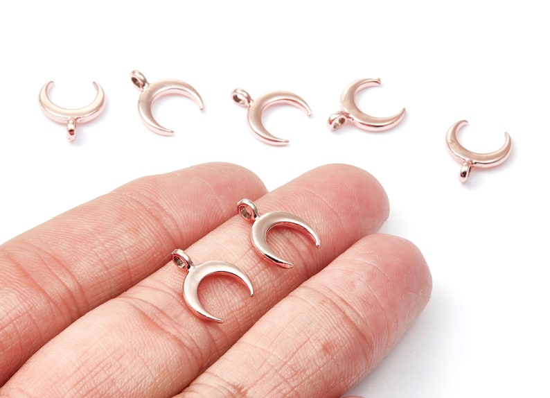 K&ouml;nnte beinhalten: Ein Set mit sechs ros&eacute;goldenen Halbmond-Anh&auml;ngern. Die Anh&auml;nger sind aus Metall und haben eine glatte, polierte Oberfl&auml;che.
