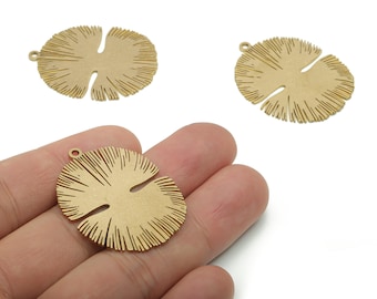 May include: Three gold-colored metal leaf-shaped pendants with a textured surface and a small loop for hanging. One pendant is held in a hand. The pendants have a botanical theme and are suitable for jewelry making.
