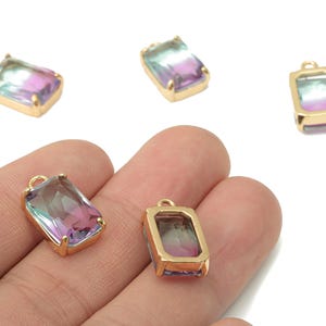 May include: Rectangular gemstone pendants with a gold-colored frame. The gemstones have a gradient of colors, including purple, teal, and pink. The pendants have a small loop at the top for attaching to a chain or other jewelry component.
