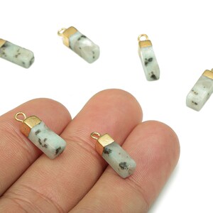 May include: Six light green gemstone pendants with gold-coloured caps. Each pendant is a rectangular shape with a small loop for attaching to a chain or other jewellery component. The gemstones have dark speckles.