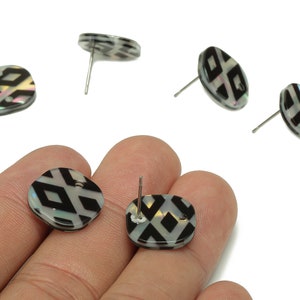 May include: A pair of black and white patterned earrings with silver posts. The earrings are made of mother of pearl and have a geometric design.
