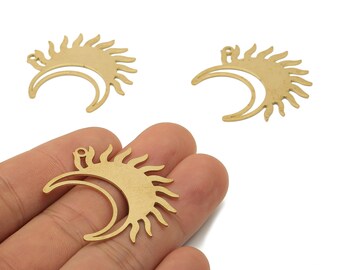 May include: Gold-colored metal charms featuring a sun and crescent moon design. The sun has pointed rays, and the moon is a curved shape. The charms are shown in a hand, suggesting their size and use in jewelry or crafts.