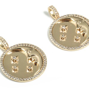 May include: Two gold pendants featuring a crescent moon design and small stars. The pendants are surrounded by a border of small clear stones.