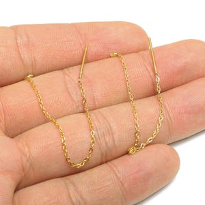 May include: A pair of gold-colored chain earrings. Each earring features a delicate chain that dangles from a straight bar. The earrings are displayed against a neutral background.