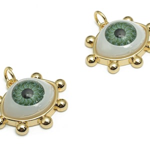 May include: Two gold-tone eye charms with green and black irises and white scleras. Each charm has a loop for attaching to a necklace or bracelet.