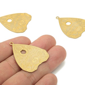 May include: Three gold-colored metal charms shaped like a triangle with a hole in the center. The charms have an etched design of a circle with a star inside, a crescent moon, and the words "Good Luck".