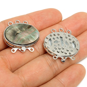 May include: Two oval-shaped jewelry clasps. One clasp features a shimmering, iridescent abalone shell design set in a silver-tone metal frame. The other clasp has a decorative, openwork design. Both clasps have loops for attaching to jewelry.