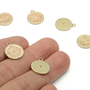 Op de afbeelding: Goudkleurige kompasbedels met een gedetailleerd ontwerp, inclusief een centrale kristal. De bedels hebben een lus om aan sieraden of andere knutselwerken te bevestigen. Verschillende bedels zijn verspreid over een wit oppervlak.