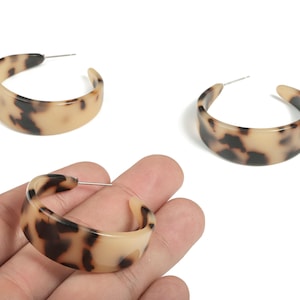 May include: Tortoiseshell hoop earrings. These earrings feature a classic tortoiseshell pattern in shades of brown and tan. The earrings are a wide, curved design with a post closure.