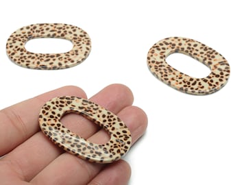 May include: Oval-shaped beads with a cream-colored base and a pattern of small, dark brown spots. The beads are shown in a close-up shot, with one held in a hand and two others nearby. These beads are suitable for jewelry making.
