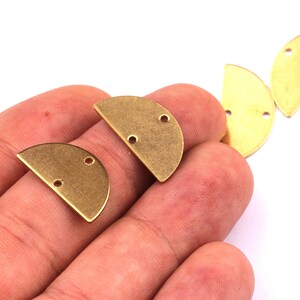 May include: Several brass-colored, half-moon shaped jewelry findings with two holes for attaching to other components. The findings are displayed against a white background.