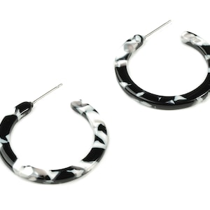 May include: A pair of black and white hoop earrings with a marbled pattern.