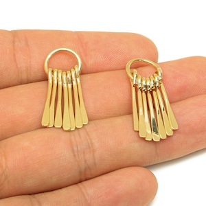 May include: A pair of gold-coloured earrings, each with a small hoop and a series of dangling, elongated rectangular shapes. The earrings are shown against a neutral background.