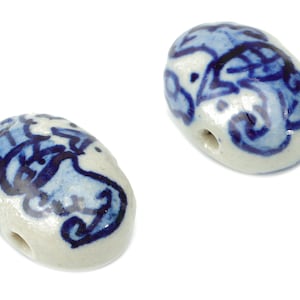 Puede incluir: Dos cuentas de cerámica blanca con diseños florales azules y blancos. Las cuentas tienen un agujero en el centro.