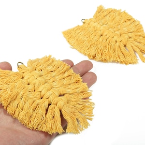 May include: Two yellow macrame earrings with a fan-like shape. The earrings are made of woven cotton and have a fringe detail. Each earring has a small metal loop at the top for hanging. The earrings are displayed on a white background.