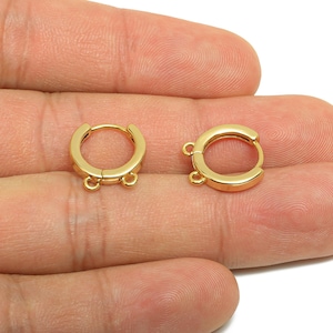 May include: Two gold-coloured hoop earrings, each with small loops for attaching charms or other jewellery components. The earrings are displayed against a neutral background.