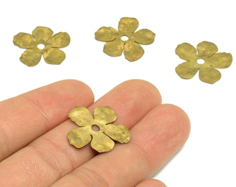 Può includere: Quattro componenti a forma di fiore in ottone con un foro centrale. Uno è tenuto in mano, mentre altri tre sono sparsi su una superficie bianca. I componenti hanno una finitura opaca, probabilmente per la creazione di gioielli o progetti artigianali.