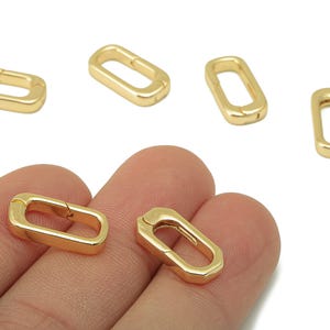 Puede incluir: Cierres rectangulares dorados. Estos componentes de joyería se muestran en una vista de primer plano, con varios cierres dispersos por la imagen. Los cierres están hechos de un material metálico brillante y están diseñados para conectar piezas de joyería.