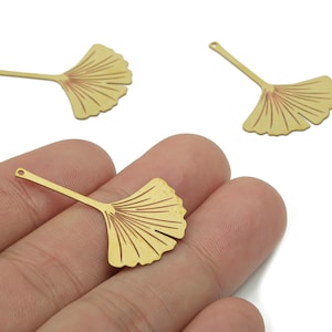 May include: Gold-colored metal Ginkgo leaf charms. The charms have a detailed leaf design with a small hole at the end of the stem for stringing. These charms are ideal for jewelry making and crafting projects.