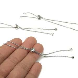 May include: Silver-toned adjustable bracelet findings. Each finding features a small, round disc with two delicate chains ending in small, round beads. The findings are designed for jewelry making and crafting.