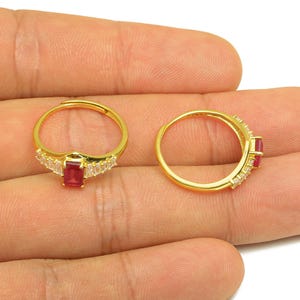 May include: Two gold rings with red and white gemstones. One ring has a rectangular red stone with white stones either side. The other ring has a red stone and white stones on the band.