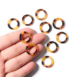 May include: A collection of ten brown and yellow patterned plastic rings. The rings are all the same size and shape, and they are arranged in a semi-circle on a white surface.