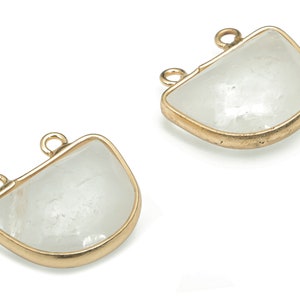 Può includere: Due ciondoli in metallo dorato a forma di mezzaluna con inserti in pietra bianca trasparente. Ogni ciondolo ha due anelli per fissarlo a una catena o un cordoncino.