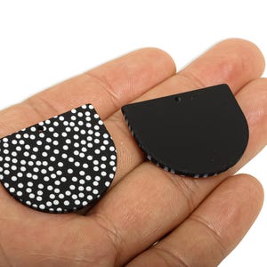 May include: Two black, semi-circular pendants. One has a white polka dot pattern, the other is solid black. Each has a small hole at the top for stringing. These pendants are likely for jewellery making.