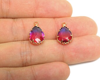 May include: Two teardrop-shaped pendants with a gold-colored filigree setting. The faceted crystals transition from a deep red to purple. Each pendant has a small loop at the top for attaching to a chain or other jewelry component.
