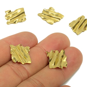 Op de afbeelding: Goudkleurige metalen bedels met een getextureerd, geribbeld ontwerp. De vierkante bedels hebben een klein gaatje aan de bovenkant om te rijgen. Verschillende bedels zijn verspreid op een witte achtergrond, met twee in een hand.