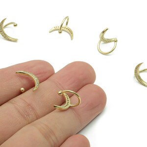 May include: Gold-colored crescent moon ear cuffs with small, clear gemstones. The ear cuffs are in various positions, showcasing their design. The jewelry is on a white background.