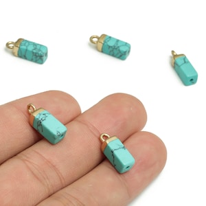 Peut inclure: Perles de pierres précieuses rectangulaires turquoise avec des capuchons et des boucles en métal doré. Les perles ont un aspect veiné naturel. Plusieurs perles sont dispersées sur fond blanc, dont une tenue dans une main.
