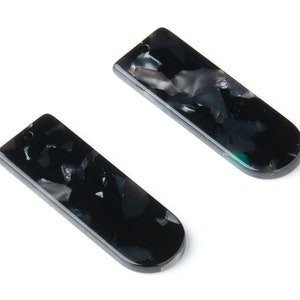 Puede incluir: Dos piezas ovaladas de plástico marmoleado en blanco y negro con un agujero en la parte superior.