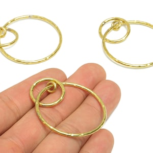 May include: Gold-colored metal jewelry components. Each piece features a large, textured oval ring connected to a smaller, round ring. The design is simple and elegant, suitable for earrings or pendants.