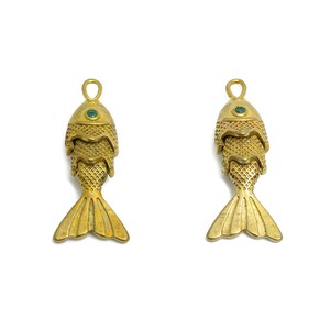 May include: Two gold-colored fish charms with green gemstone eyes. The fish are stacked on top of each other and have a detailed, textured design.