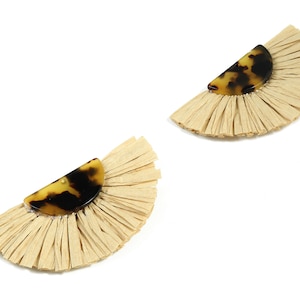 May include: A pair of half-circle earrings. Each earring has a tortoiseshell-patterned semi-circle above a fan of beige raffia. The raffia fans have a textured, fringed appearance. The earrings are set against a white background.
