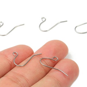 May include: Silver earring hooks in various positions. Three hooks are arranged at the top, while two are held by a hand at the bottom. The hooks have a curved design with a small loop at the top.